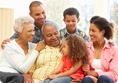 Several generations of an African American family laughing and being social while sitting on a couch in their living room