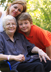 Mother is sitting in chair with her daughter and grandson bending down next to her. Their faces are touching.