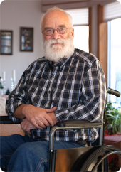 Senior man sitting in a wheelchair with sunlit window behind him