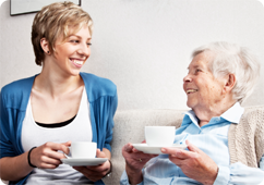 Young women laughing with an older women while holding a cup of tea.